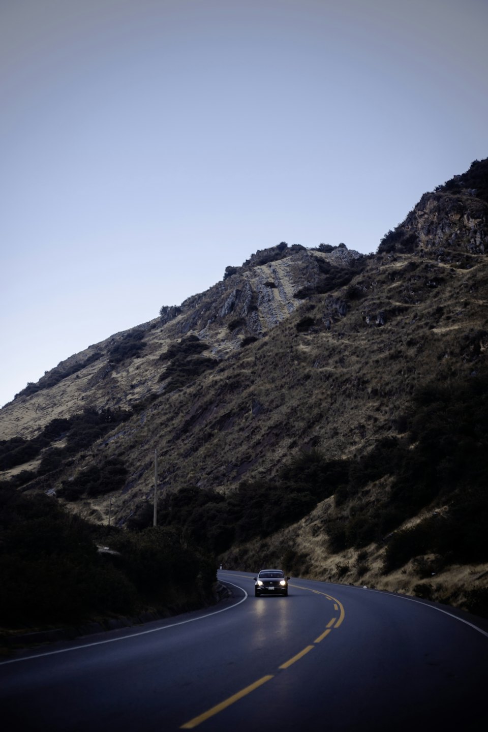 Los faros de un coche iluminan una carretera de montaña sinuosa al anochecer.