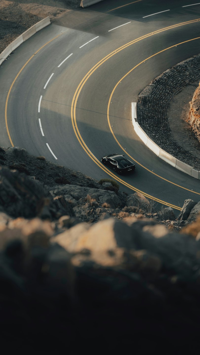 Un coche deportivo negro circula por una carretera de montaña serpenteante.